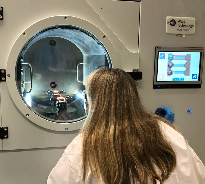 A Fingerprint Specialist observes latent fingerprints develop in the Vacuum Metal Deposition (VMD) chamber. VMD assists in extreme case scenarios such as cold cases, homicides, and more.